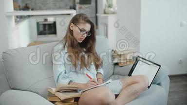 戴眼镜的少女在笔记本上看书，看屏幕，在笔记本上写字，准备考试